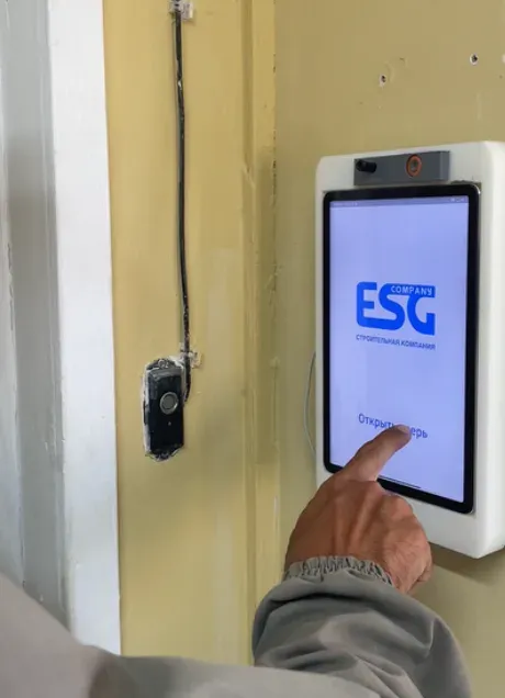 A finger pressing the button 'Открыть дверь', open the door, on a white wall tablet whose screen shows the ESG company logo