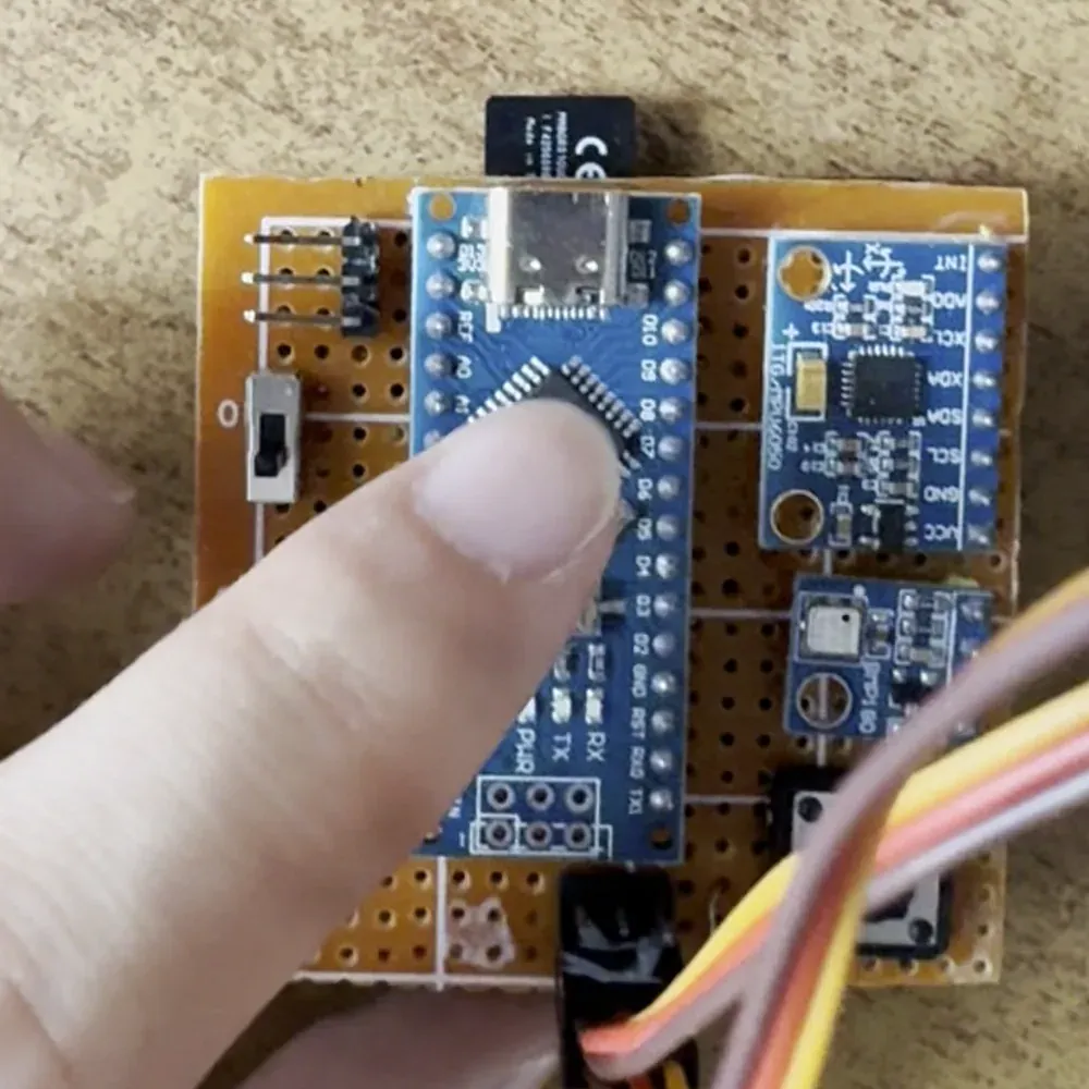 Top-down view of the avionics perfboard: an Arduino Nano, sensor boards and servo leads, a finger pointing at the Nano