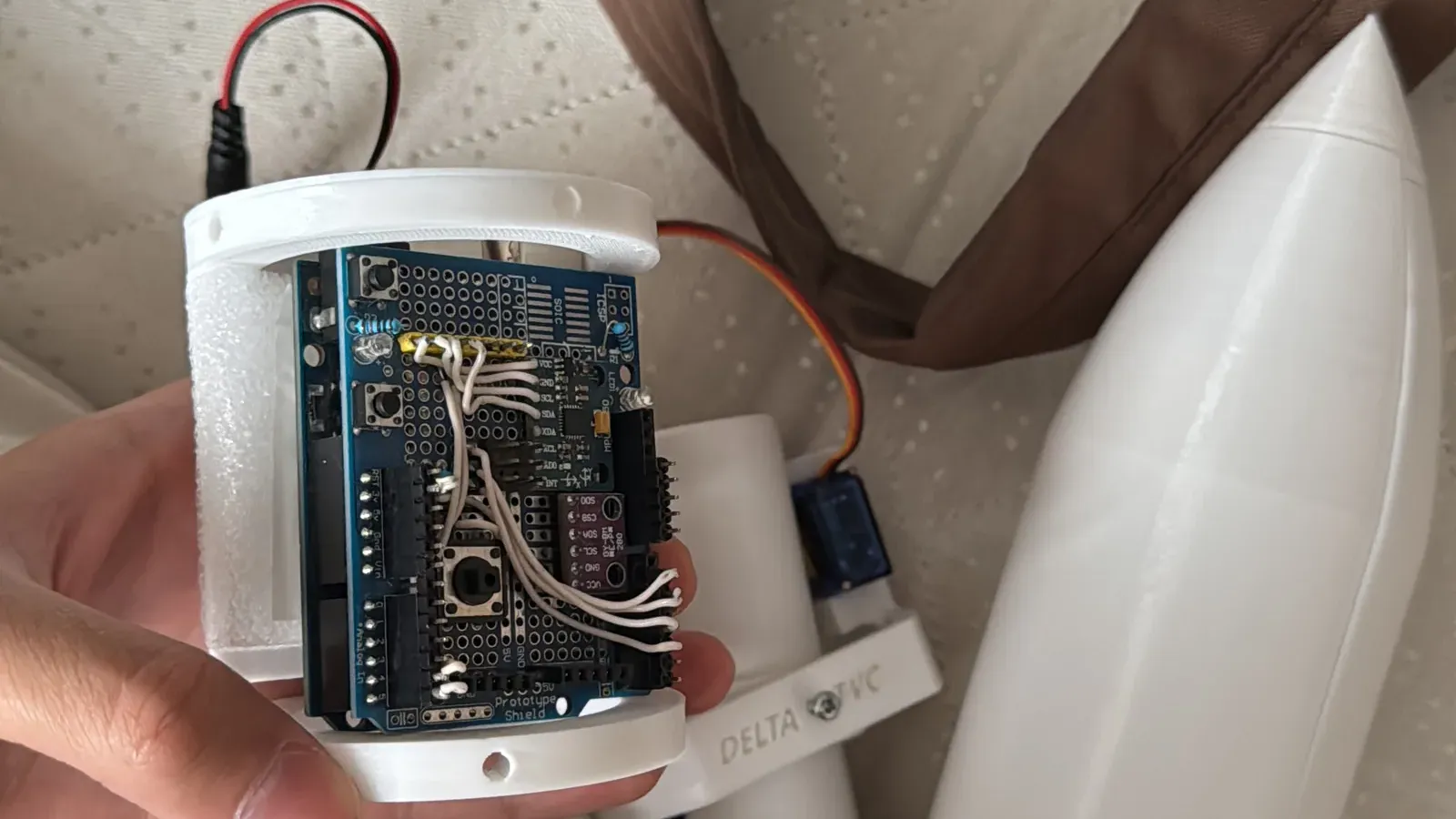 The printed avionics bay held open in one hand, wired boards inside, with the servo mount and the white nose cone beside it