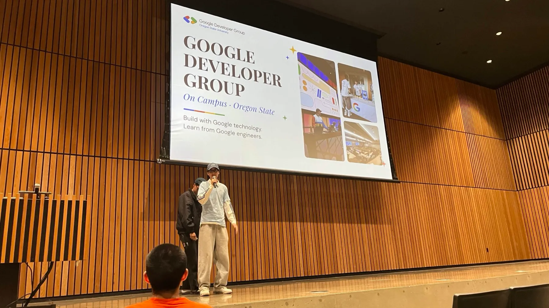 Jak with a microphone on the same stage, under the chapter's title slide: 'Google Developer Group, On Campus · Oregon State', with the lines 'Build with Google technology' and 'Learn from Google engineers'