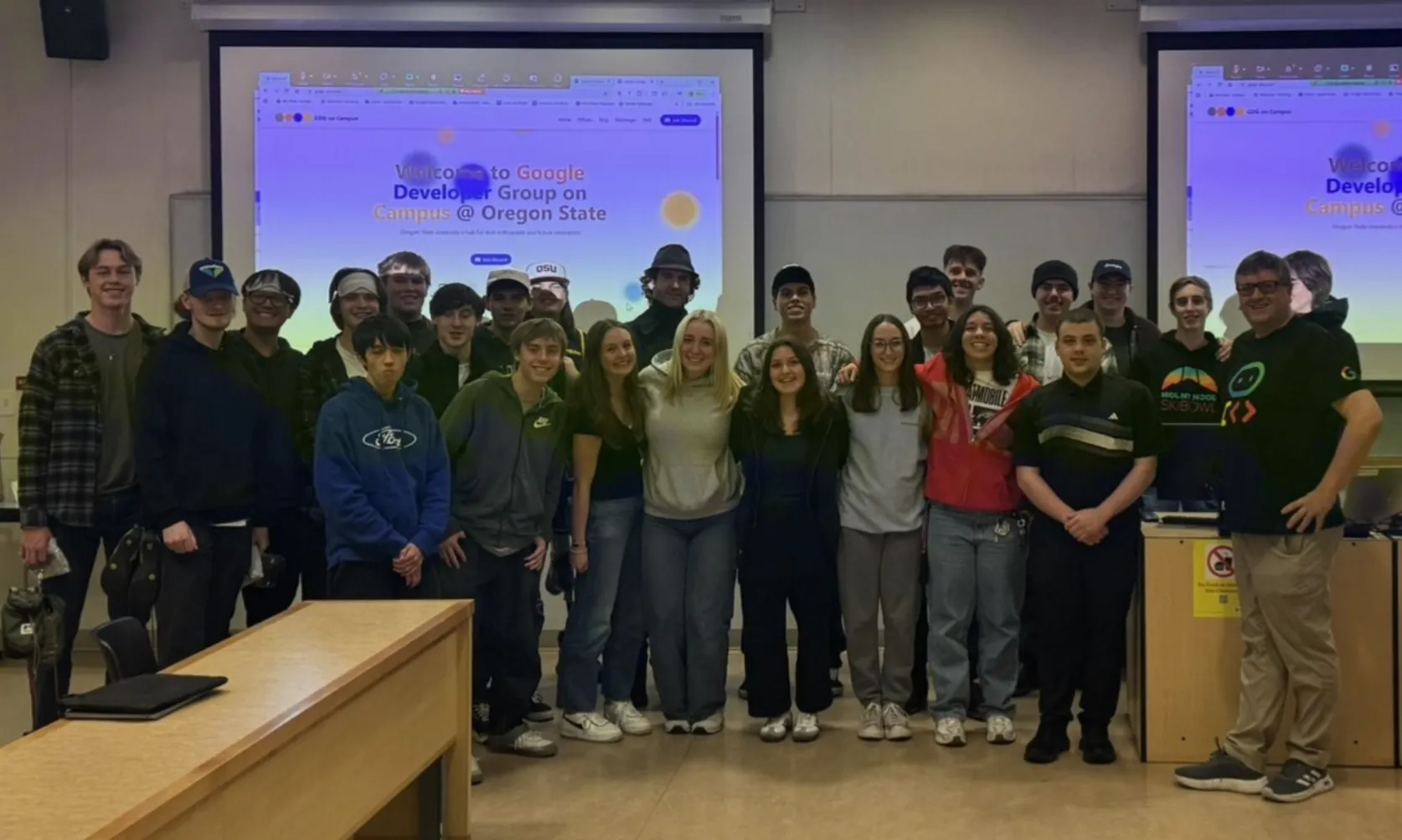 A group of students posed together in a lecture room, under a projected screen that reads 'Welcome to Google Developer Group on Campus @ Oregon State'