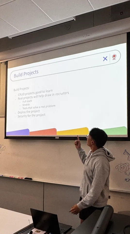 A student pointing up at a projected slide titled 'Build Projects'