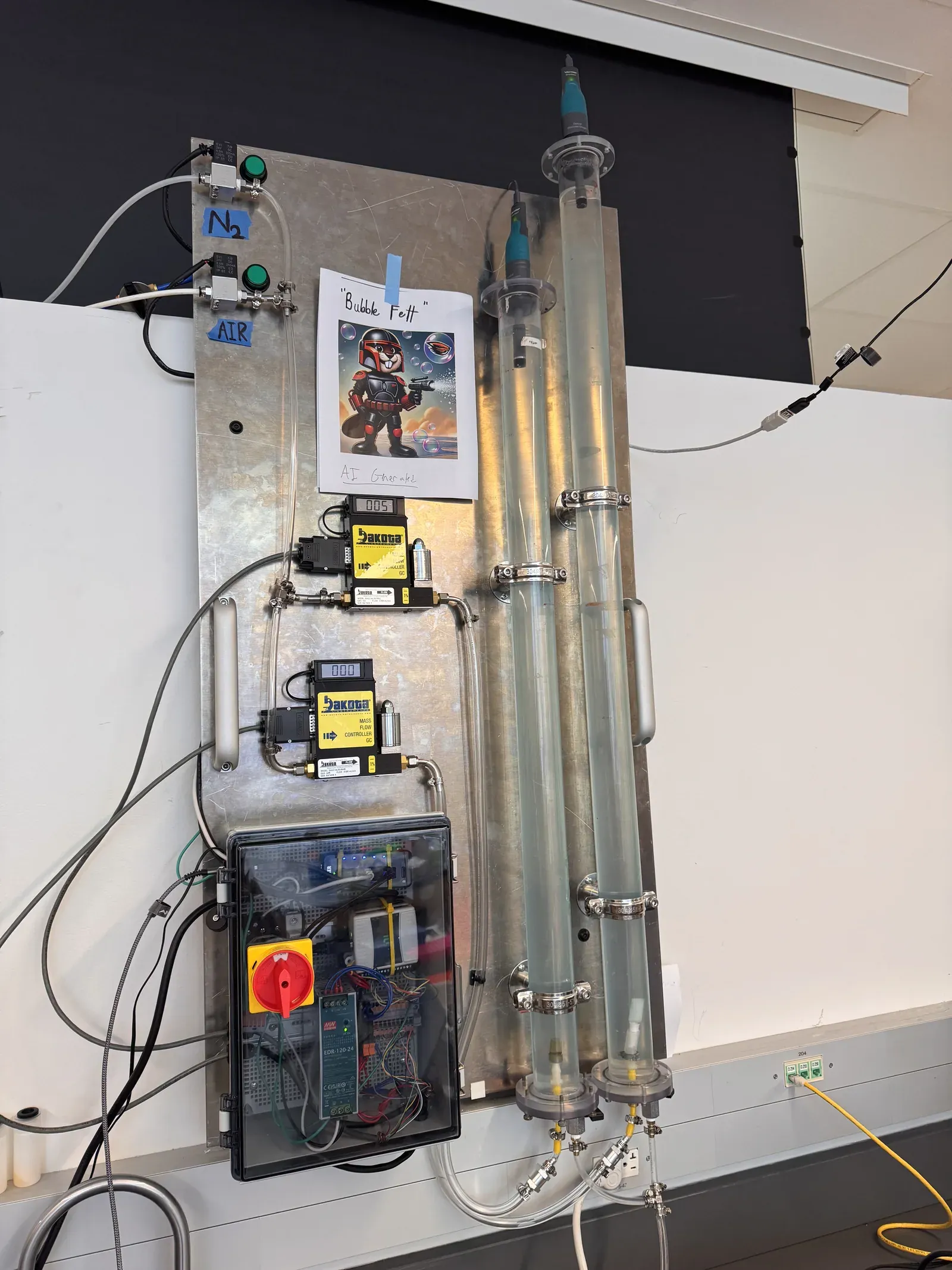 Rig one on a steel panel: nitrogen and air valves, two mass-flow controllers, a control box with a red switch, and two clear columns with probes