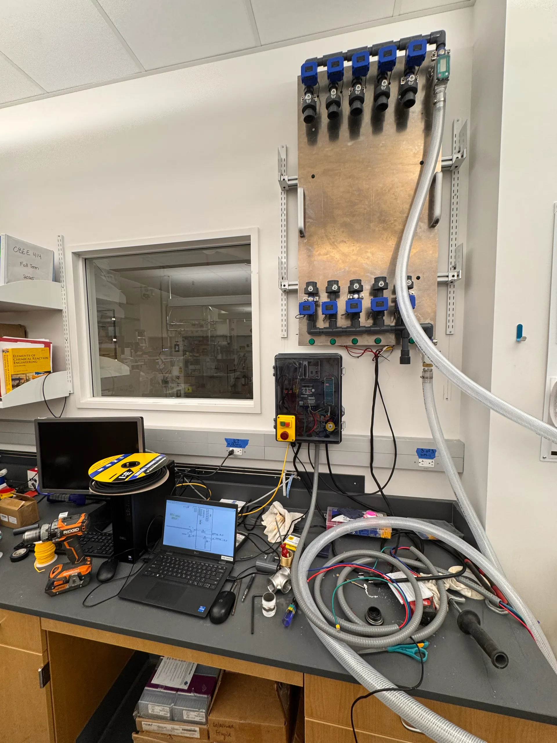 Rig two: a wall panel of blue sensor fittings above a control box with an emergency stop, and a laptop on the bench below