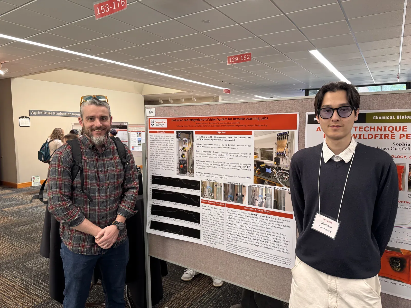 Jakhangir standing beside his research poster in a hall of posters, a man on its other side