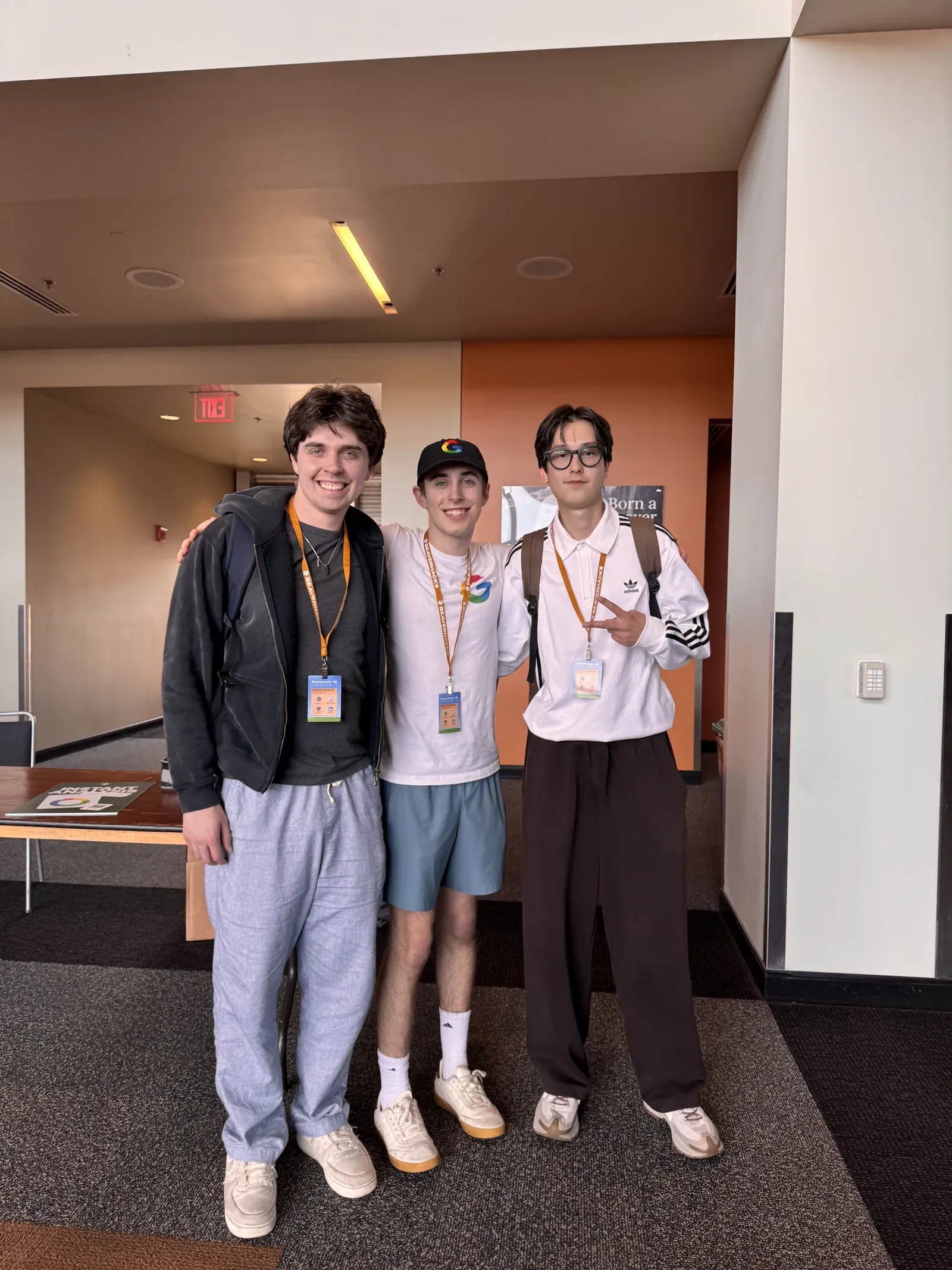 Jakhangir, his teammate Carson Secrest and the Google track presenter standing together in a hallway, event lanyards on