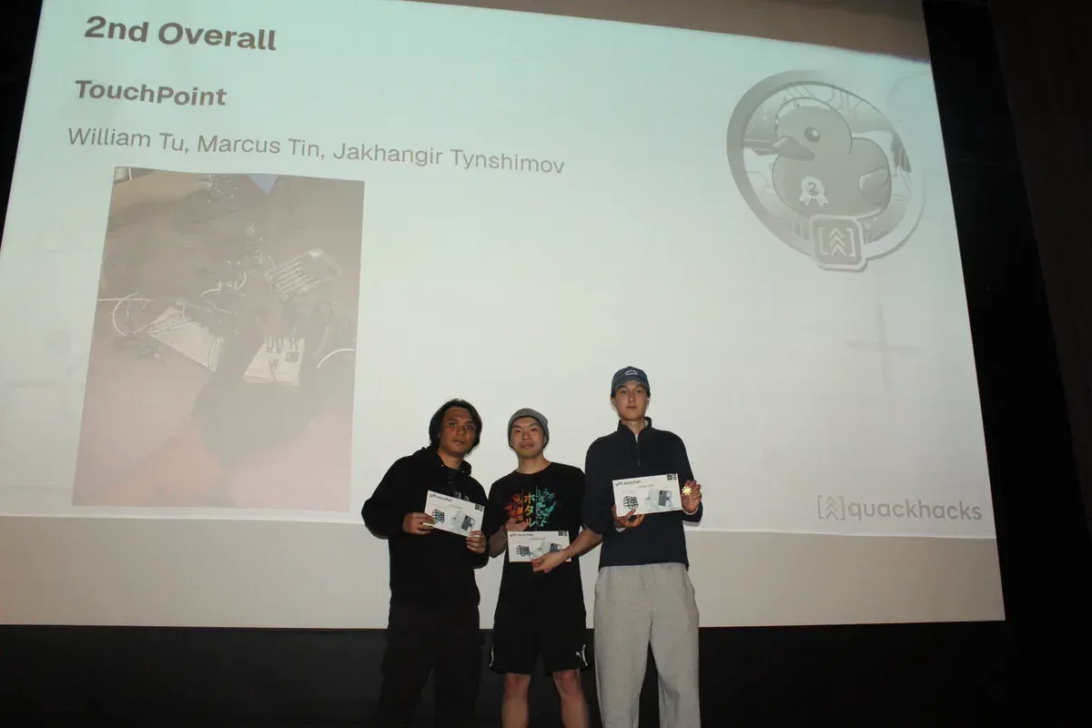 The team on stage holding their prize vouchers; the slide reads 2nd Overall, TouchPoint, with the three names