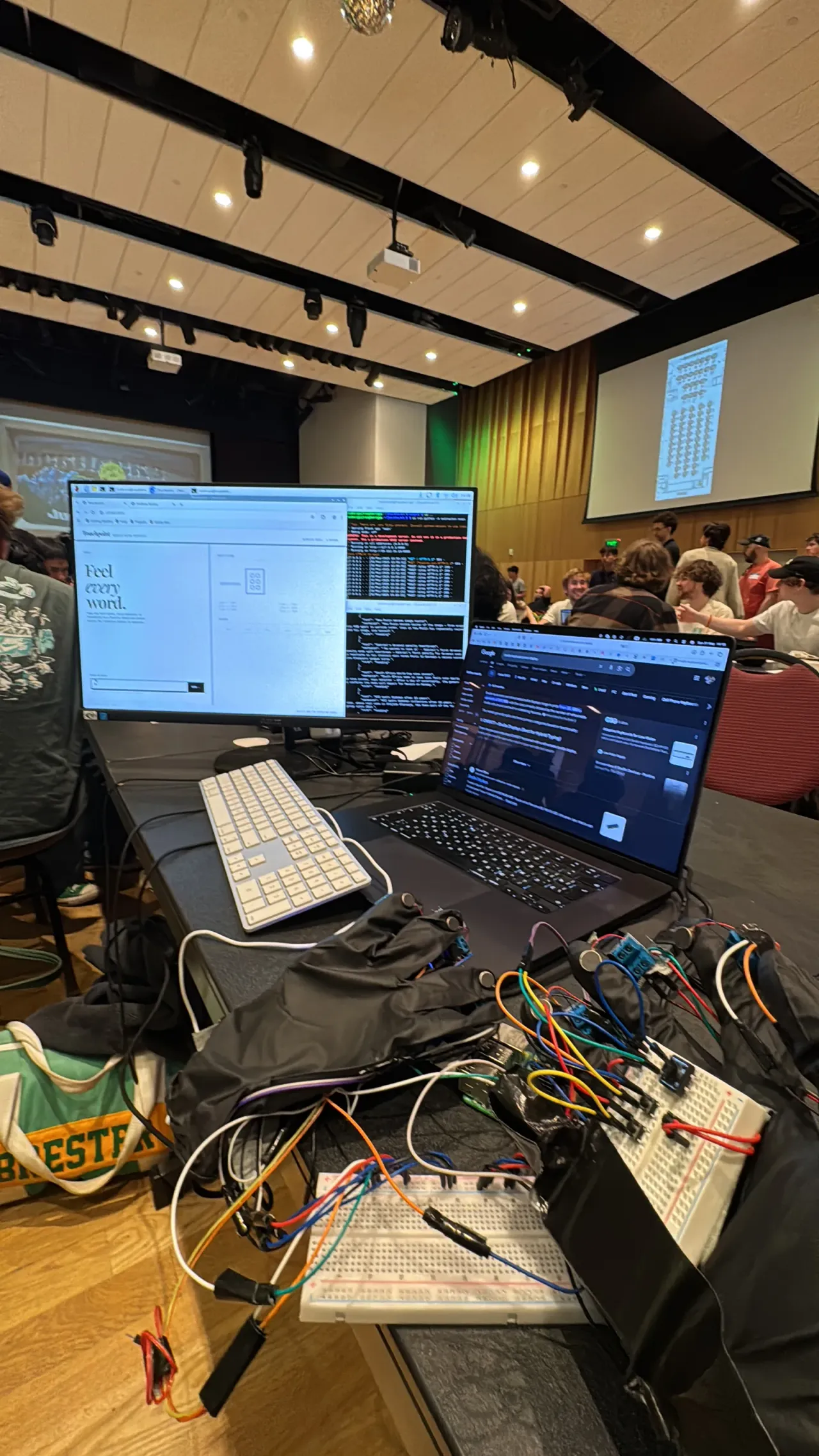 The TouchPoint web interface, 'Feel every word.', with both wired gloves on the table in the QuackHacks hall