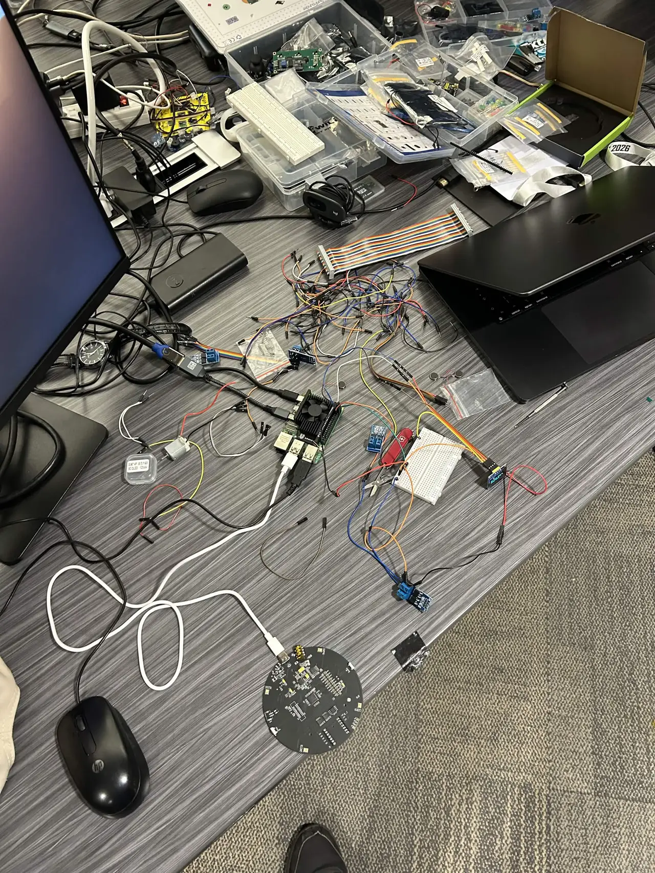 The build desk from above: the round microphone array board, microcontroller and breadboards wired together, a laptop and a mouse among the cables