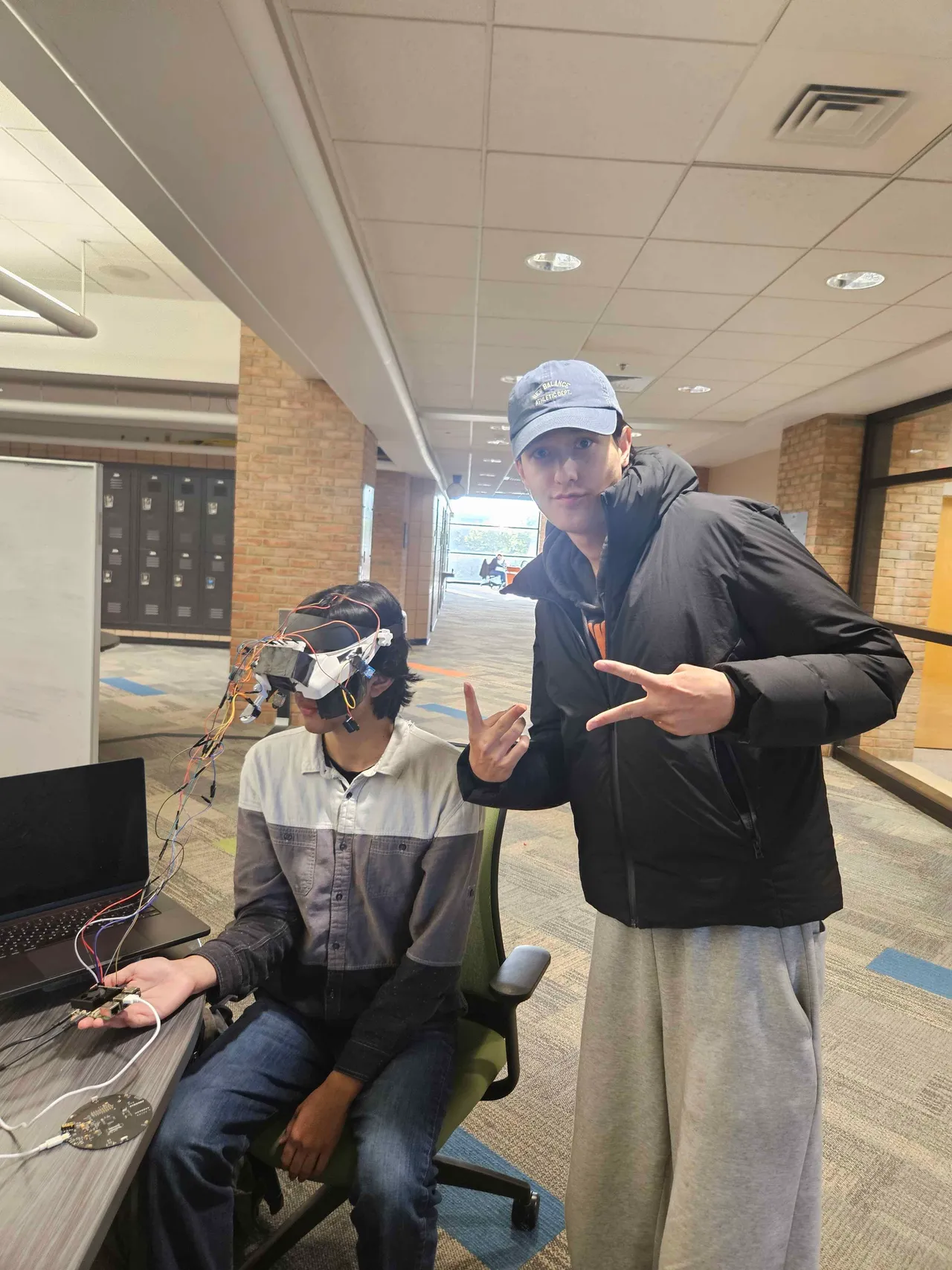 A teammate seated wearing the headset, wires running to a laptop; Jakhangir standing beside him