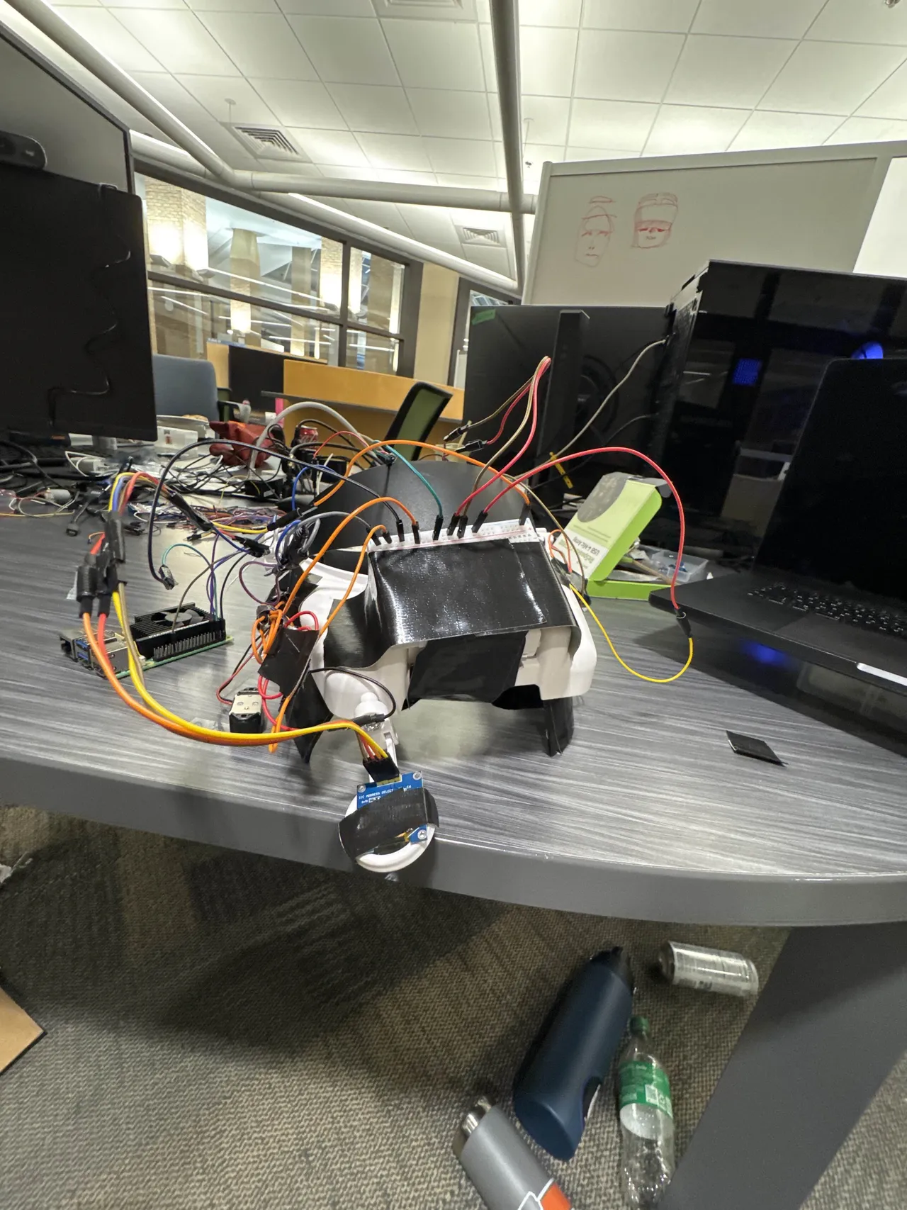 The prototype on the table: the Pi beside it, the OLED hanging on its wires, two face sketches on the whiteboard behind