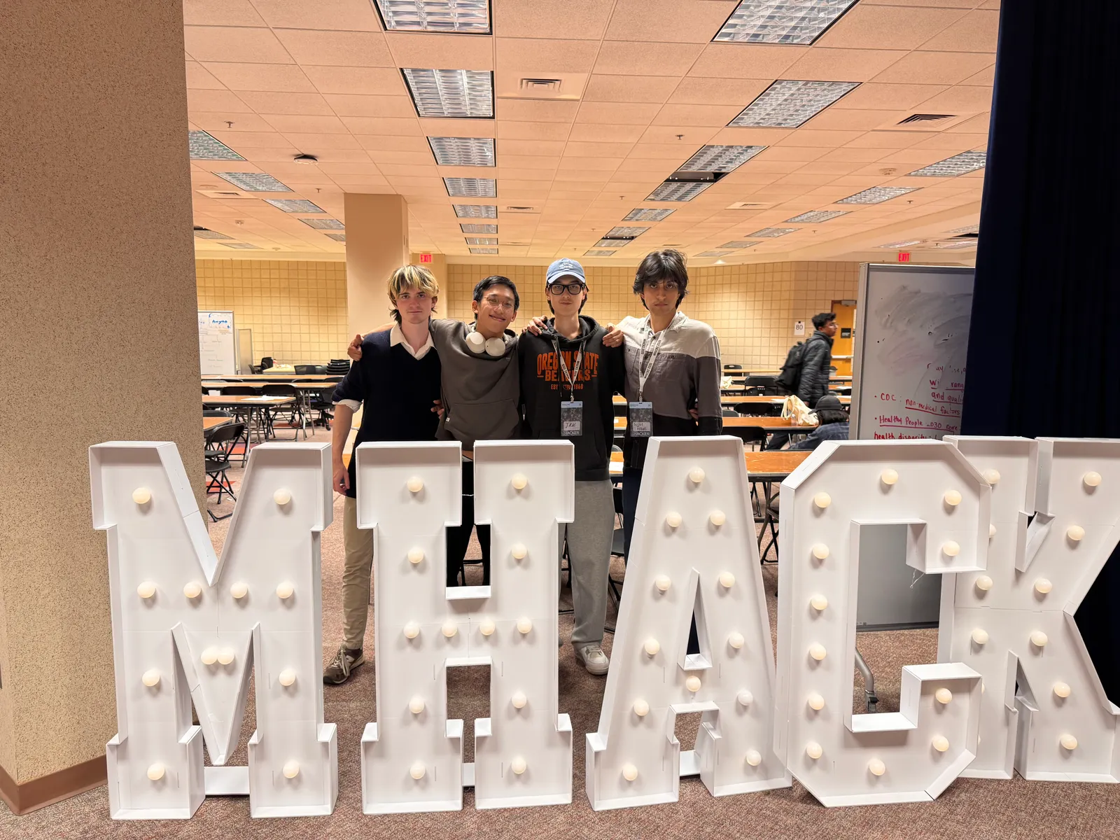 The four teammates behind the MHACKS marquee letters in the judging hall