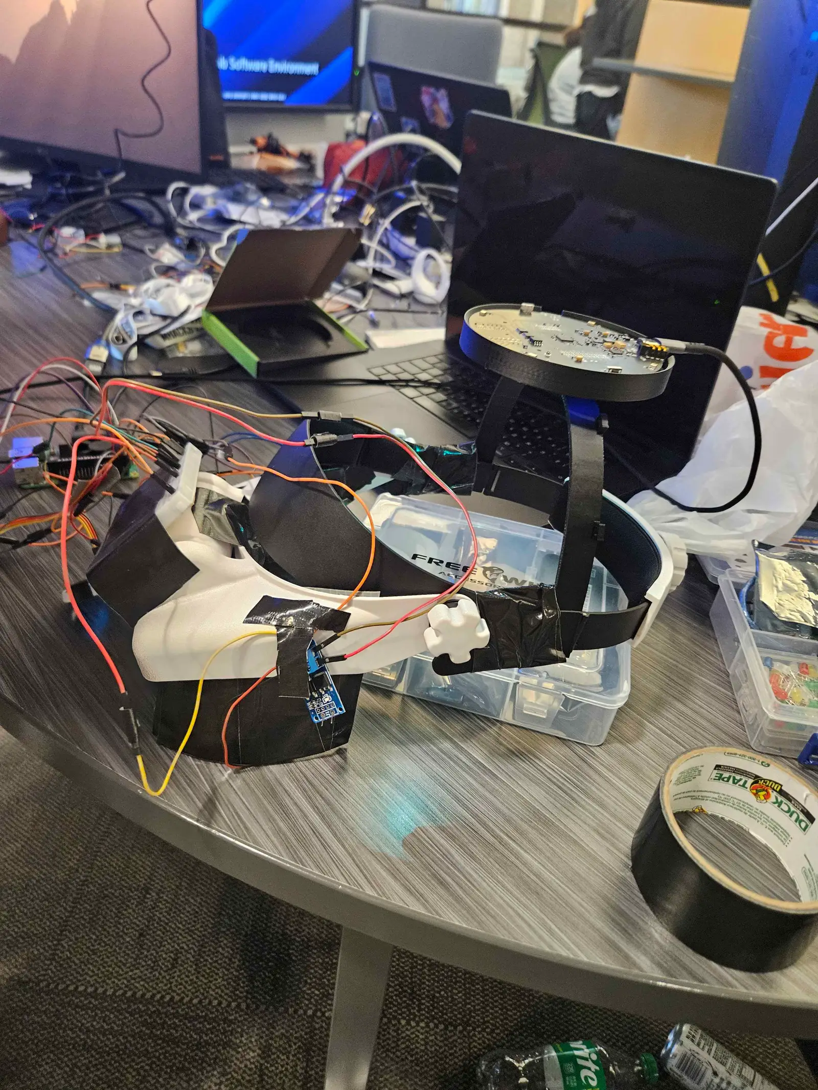 The Usher prototype on the build table: the white headset band wrapped in black tape and wired to the boards, the round microphone array on a stand above it